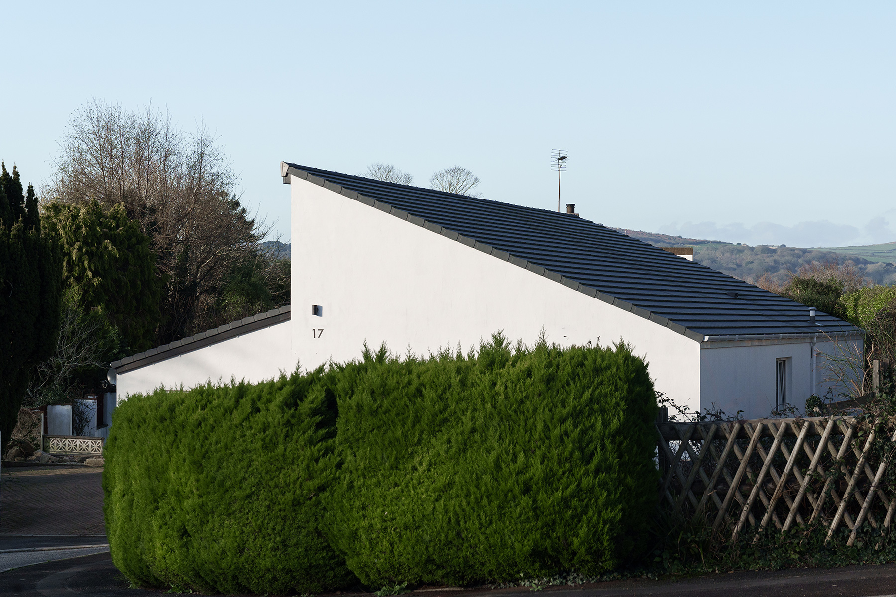 Tile roofing on a build in Cornwall; a sloping tiled roof, with hedge in foreground of image.